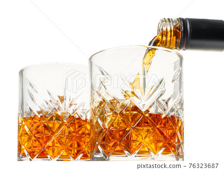 whiskey is poured into a glass from bottle 76323687