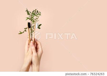 Hands hold one bamboo eco tooth brush. brown color. Dental care. Morning oral healhcare routine. Beige neutral background. Copy space. Washing prevention hygiene, zero waste, eco-friendly 76324263