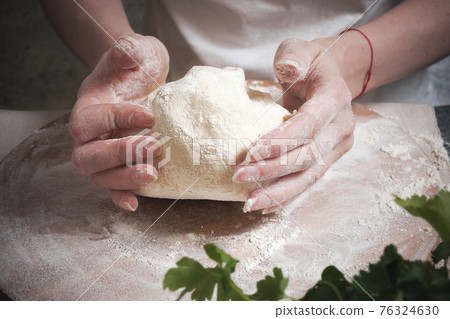 Women's hands knead the dough from wheat flour 76324630