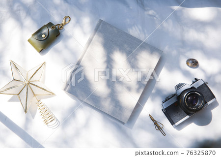 A book placed on a white fabric with natural light and the shadows of plants A book placed on a white fabric with natural light and the shadows of plants 76325870