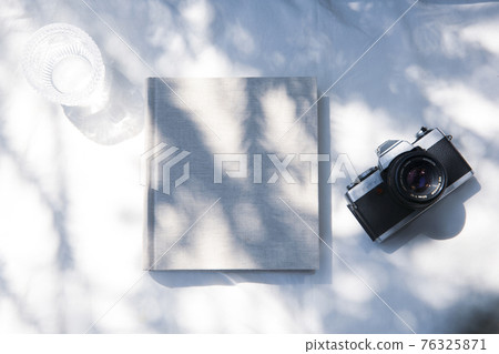 A book placed on a white fabric with natural light and the shadows of plants 76325871
