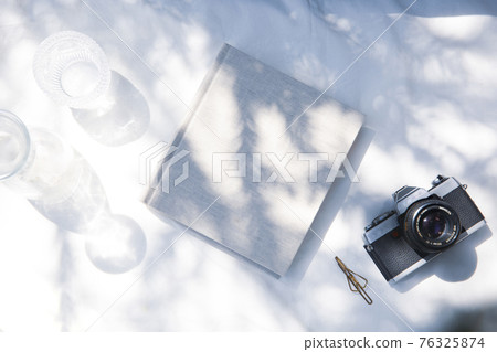 A book placed on a white fabric with natural light and the shadows of plants A book placed on a white fabric with natural light and the shadows of plants 76325874