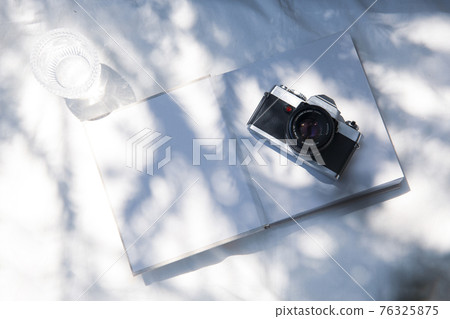 A book placed on a white fabric with natural light and the shadows of plants A book placed on a white fabric with natural light and the shadows of plants 76325875