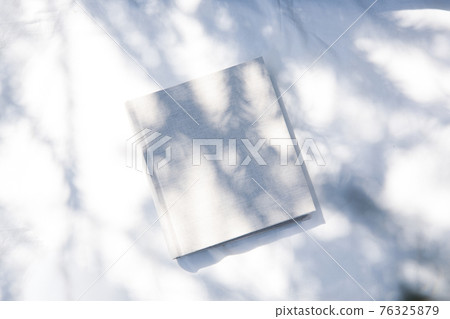 一本放在白色織物上的書，有自然光和植物的陰影 76325879