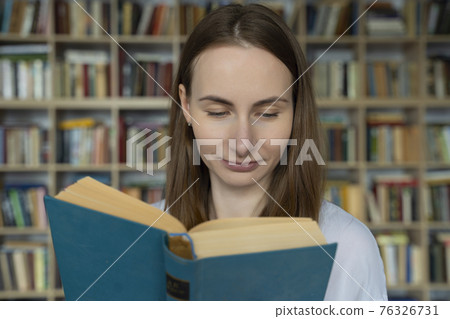 Young woman student reading a book in a library Young woman student reading a book in a library 76326731