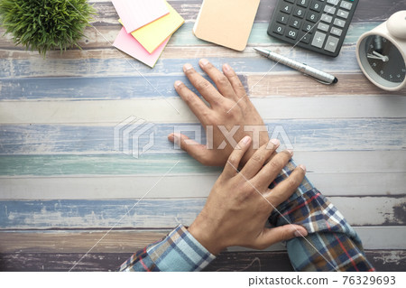 man suffering pain in hand on table with stationary man suffering pain in hand on table with stationary 76329693