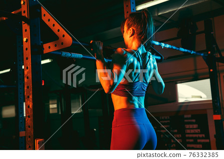 Young athletic woman, fitness instructor training in gym in mixed neon light. 76332385