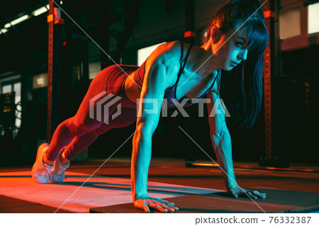 Young athletic woman, fitness instructor training in gym in mixed neon light. 76332387