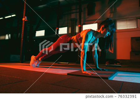 Young athletic woman, fitness instructor training in gym in mixed neon light. 76332391