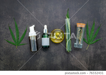 Glass bottle of cannabis oil and hemp leaves set up  on concrete background. 76332431