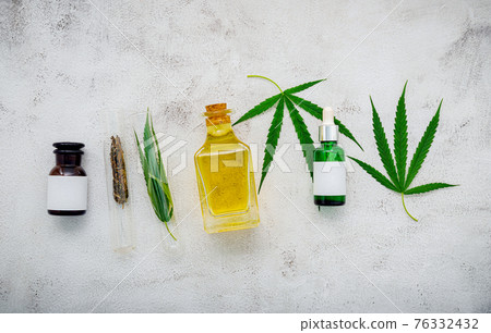 Glass bottle of cannabis oil and hemp leaves set up  on concrete background. 76332432