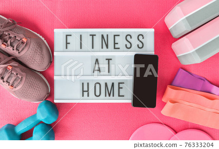 Fitness at home sign with mobile phone on pink yoga mat, running shoes, kettlebell weight and dumbells resistance bands and sliders for pilates online class. Exercise indoors for women. 76333204