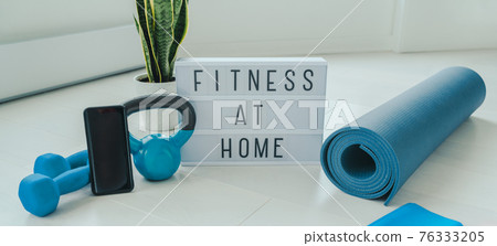 Fitness at home lightbox sign in living room for online workout on phone app training indoors with dumbbell weights and resistance bands on yoga mat banner background. Fitness at home lightbox sign in living room for online workout on phone app training indoors with dumbbell weights and resistance bands on yoga mat banner background. 76333205