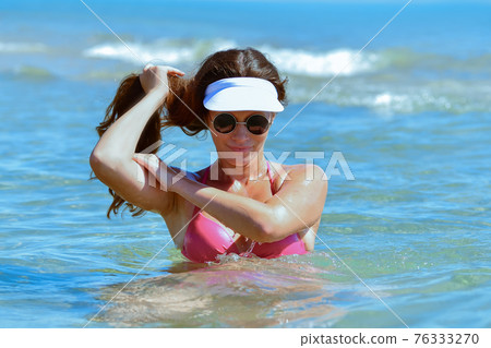 woman wearing glasses and a sun visor holding her hair while enjoying the sea waters 76333270