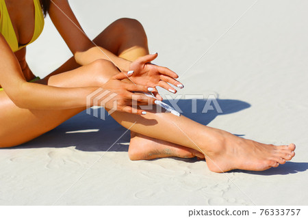Woman's beautiful legs on the beach. Tan Woman Applying Sunscreen on Legs. Close-up Woman's beautiful legs on the beach. Tan Woman Applying Sunscreen on Legs. Close-up 76333757