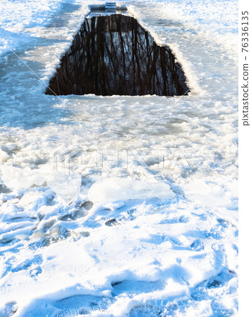 long ice-hole in frozen snow-covered river 76336135