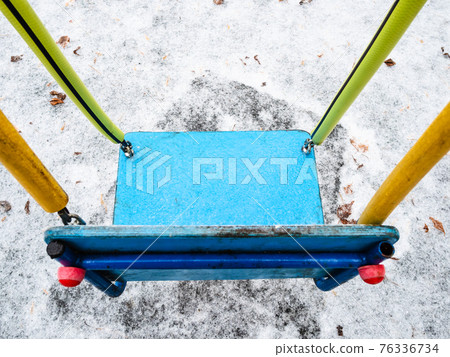 ice-covered seat of swing on children playground 76336734