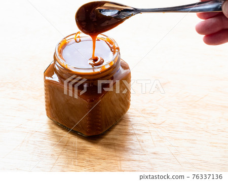 cooking salted butter caramel sauce at home kitchen - homemade smooth cooked salty caramel dessert in open glass jar on wooden board 76337136