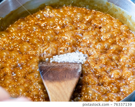 cooking salted butter caramel sauce at home kitchen - adding coarse sea salt in boiling melted sugar, butter and cream in steel pan close up 76337139