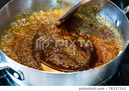 cooking salted butter caramel sauce at home kitchen - mixing boiled mixture of sugar and butter with wooden culinary spatula in steel pan close up 76337142