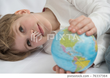 The child dreamily examines the globe. Travel yearning concept. Closed borders and quarantine. A European-looking child dreams of travel 76337364