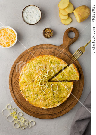 Quiche pie with leek, potatoes and cheese flat lay on gray concrete background and ingredients cheese, sour cream, onion rings on round wooden cutting board 76338033