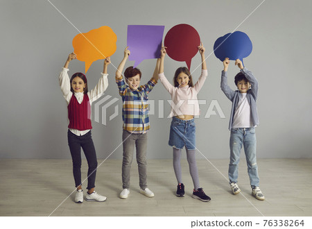 Group of happy little school children holding up multicolored paper speech balloons Group of happy little school children holding up multicolored paper speech balloons 76338264
