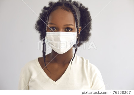 Studio headshot of a young African woman wearing a disposable surgical face mask Studio headshot of a young African woman wearing a disposable surgical face mask 76338267