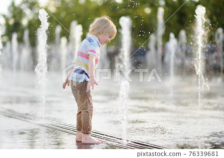 Little boy plays in the square between the water jets in the dry fountain at sunny summer day. 76339681