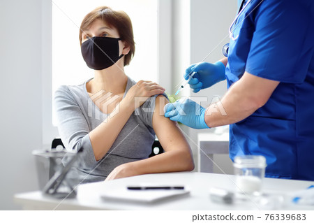 Doctor or nurse is preparing to give a injection vaccine against covid-19 to a woman. Mass vaccination. Herd immunity 76339683
