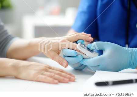 A woman at a doctor's appointment during the coronavirus epidemic. Doctor checking oxygenation with fingertip pulse oximeter. Saturation blood of oxygen. 76339684