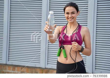 Attractive young lady posing with jumping-rope and bottle of water Attractive young lady posing with jumping-rope and bottle of water 76339986