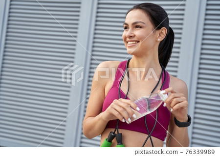 Smiling sporty brunette opening a water bottle Smiling sporty brunette opening a water bottle 76339989
