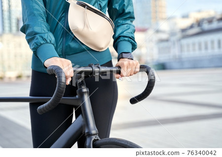 Woman in a sports jacket and leggings with a bicycle in the city Woman in a sports jacket and leggings with a bicycle in the city 76340042