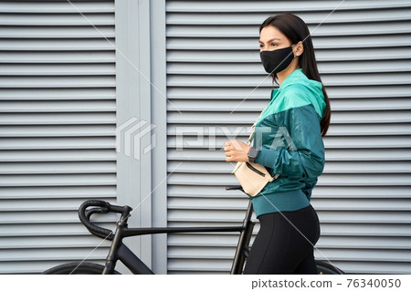 Sporty lady standing near the bike and looking in front of her Sporty lady standing near the bike and looking in front of her 76340050