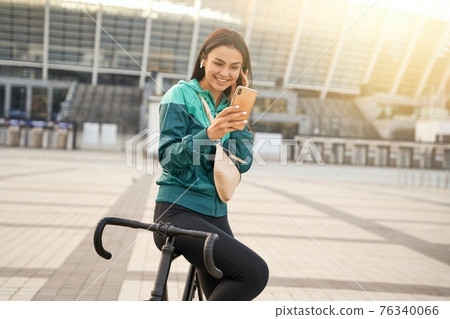 Brunette athletic woman using mobile phone and wireless headphones 76340066