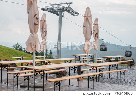 Closed umbrellas in the cafe in mountains on the background of cable car road during pandemic of coronavirus.  76340966