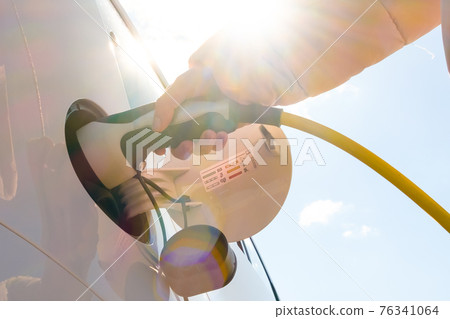 Close up woman hand inserts power cable supply to charge electric or EV car at sunlight  76341064