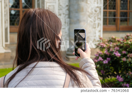 Young woman or blogger in face mask shooting video of castle on her smartphone in spring. Tourism during pandemic 76341068