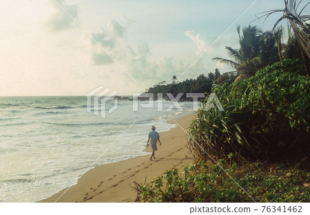 A traditonally dressed man walks by the sea at Negombo beach in Sri Lanka. Retro 1993 film capture. A traditonally dressed man walks by the sea at Negombo beach in Sri Lanka. Retro 1993 film capture. 76341462