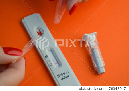 test for coronavirus on an orange background. sensitive strip, a girl with a bright red manicure drips on a drop of blood for a test. there is a lancet for piercing a finger test for coronavirus on an orange background. sensitive strip, a girl with a bright red manicure drips on a drop of blood for a test. there is a lancet for piercing a finger 76342947