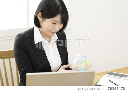 A woman looking at a globe at her desk A woman looking at a globe at her desk 76343478