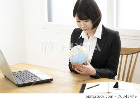 一個女人看著她的辦公桌上的地球儀 一個女人看著她的辦公桌上的地球儀 76343479