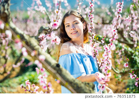 Portrait of young smiling woman in a garden with blooming peach Portrait of young smiling woman in a garden with blooming peach 76351875