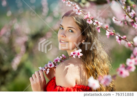 Cheerful girl posing in a red dress in spring blooming garde Cheerful girl posing in a red dress in spring blooming garde 76351888