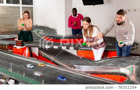 Cheerful men and women play together with slot car racing track 76352104