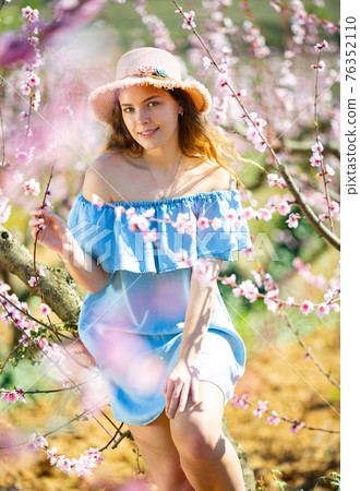 Lovely girl in hat and blue dress in peach garden Lovely girl in hat and blue dress in peach garden 76352110