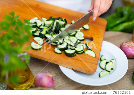 Slicing fresh cucumber on cutting board 76352161