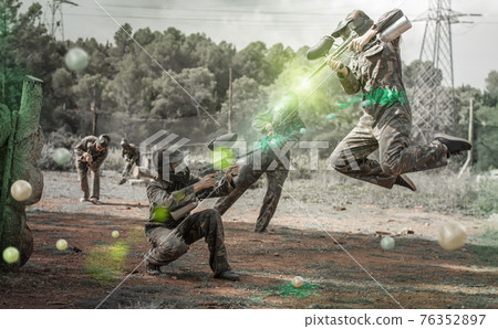 Dynamic paintball battle. Portrait woman player jumping and aimi Dynamic paintball battle. Portrait woman player jumping and aimi 76352897