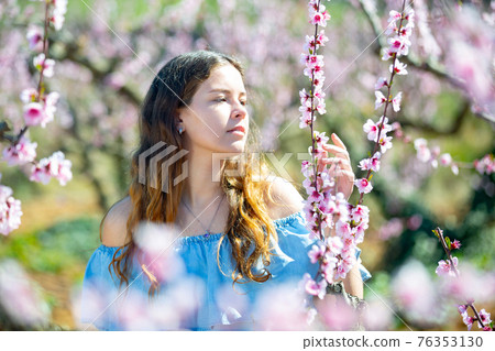 Young smiling lady posing in park with blooming trees 76353130